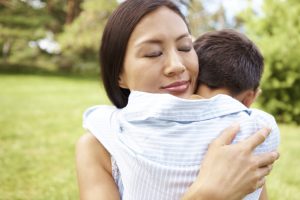 Pretty young Asian mother hugging her little boy in a park